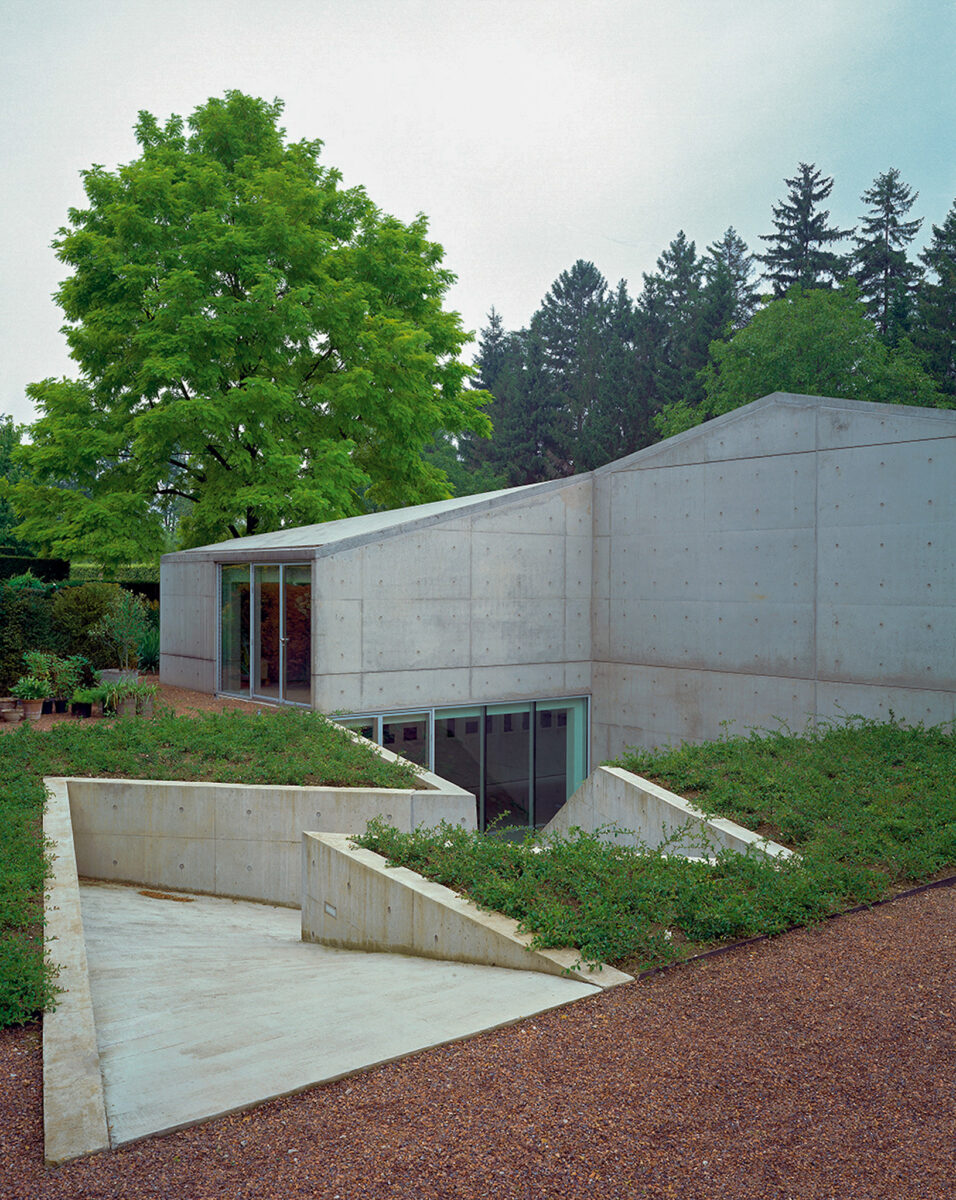 This museum building is made of cast concrete and aluminum-framed glass, and rises only a single story above the ground in the garden, matching the height of the surrounding hedges